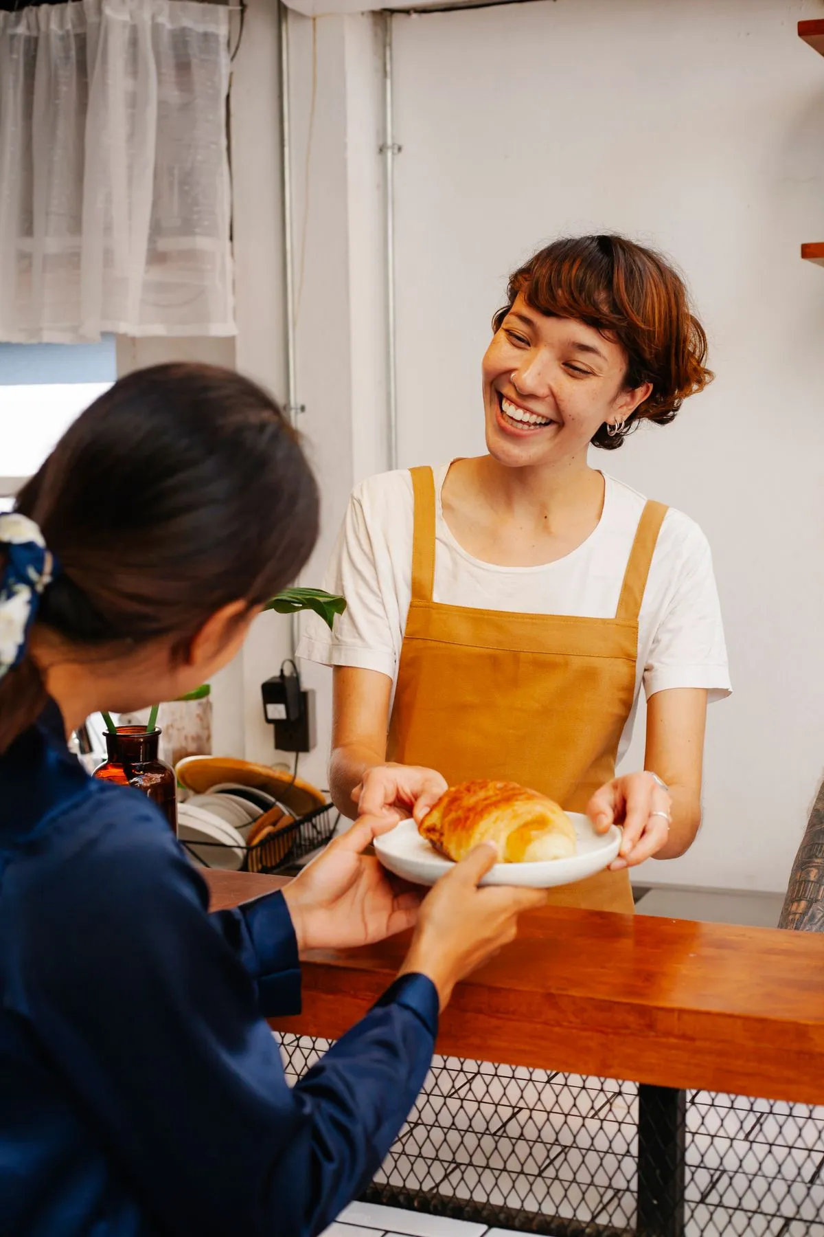 Een lachende bakkerijmedewerker overhandigt een croissant aan een klant